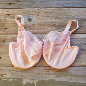 May include: A light pink bra with adjustable straps and delicate lace detailing. The bra features a full coverage design with a smooth, satin-like fabric. The lace accents are visible along the top edges of the cups.