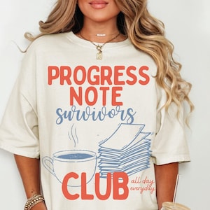 May include: Ivory-colored t-shirt with the text "PROGRESS NOTE SURVIVORS CLUB" in red and blue. The design includes a coffee cup, a stack of papers, and the words "all day everyday".