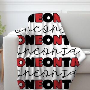 May include: White fleece throw blanket with the words "NEONTA" repeated in black and red lettering.