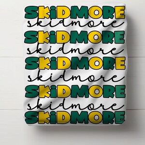 May include: White fabric with the word "SKIDMORE" repeated in green and yellow letters.