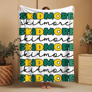 May include: White fleece blanket with the word "SKIDMORE" repeated in green and yellow lettering.