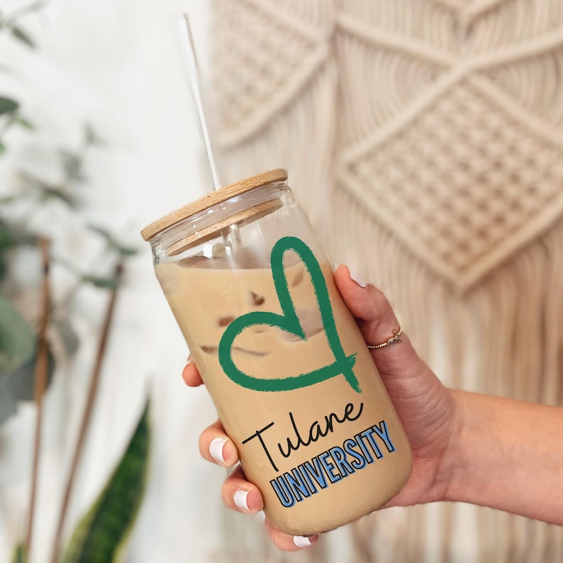 May include: A clear glass tumbler with a bamboo lid and a green heart design. The tumbler has the text "Tulane University" printed on it.