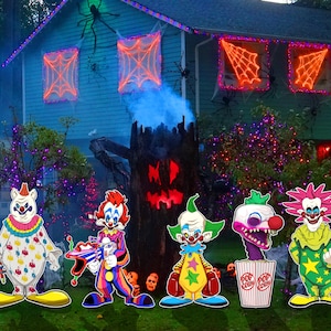 May include: Five colorful clown yard decorations with different expressions and poses. The clowns are made of wood and have a painted finish. They are standing in front of a house decorated for Halloween.