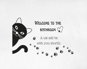 Peut inclure: Tapis de bain rectangulaire blanc avec un chat noir et le texte "WELCOME TO THE BATHROOM" et "A cat will be with you shortly." Des chaussons en tricot gris sont au premier plan.