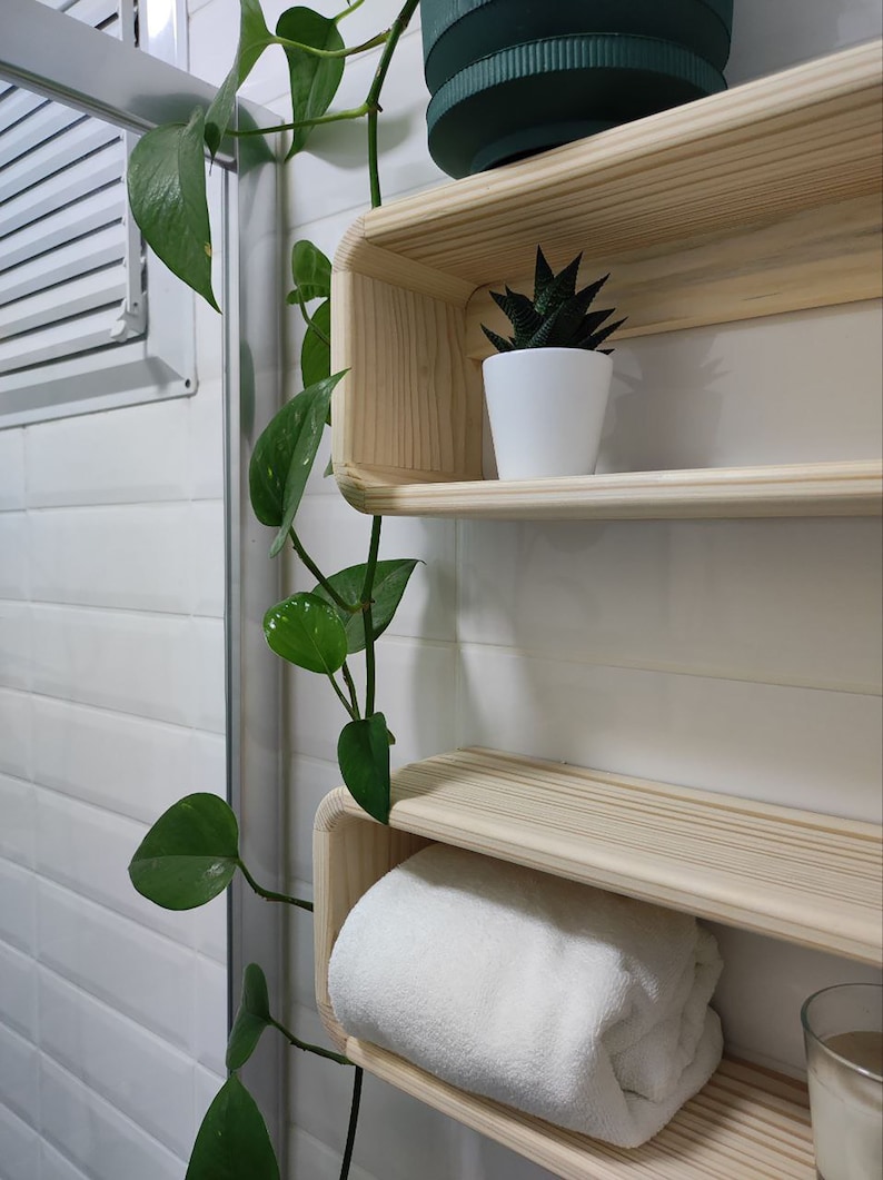May include: Two wooden shelves with rounded edges, mounted on a white tiled wall. The top shelf has a small potted succulent plant, and the bottom shelf has a white towel folded on it.