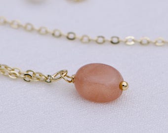 May include: A delicate gold chain necklace with a single, light pink, oval-shaped gemstone pendant.