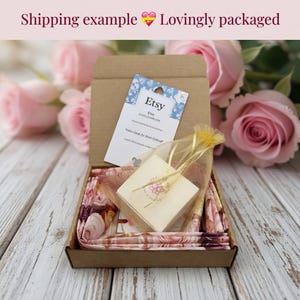 May include: A brown cardboard box filled with a floral patterned fabric, a small gift box, and a tag that says "Etsy". The background features pink roses and a wooden surface.