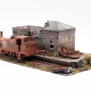 May include: A detailed model of a rusty, vintage steam train and station. The train is a weathered orange-brown colour, with visible rust. The station building is grey with a partially collapsed roof and the text "KBG".