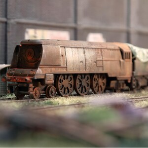 May include: A detailed model steam train, with a rusty brown finish, set on miniature tracks. The train has large wheels and a prominent front section, with a covered cargo car at the rear. The model evokes a sense of vintage railway history.