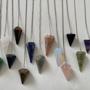 Może przedstawiać: Zestaw 12 kryształowych wahadeł ze srebrnymi łańcuszkami. Wahadła wykonane są z różnych kryształów, w tym ametystu, różowego kwarcu, czystego kwarcu i zielonego awenturynu.