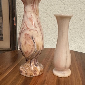 May include: Two decorative vases made of pink and white marble. The larger vase has a swirling pattern and a wider base. The smaller vase is a simple, slender design.