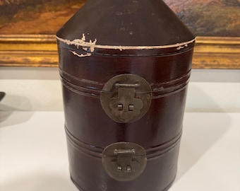 May include: A dark brown wooden box with a conical lid and two metal clasps. The box has a distressed finish and is decorated with a simple design.
