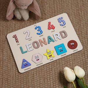 Może przedstawiać: Drewniana zabawka edukacyjna z kolorowymi liczbami, literami i kształtami. Zabawka zawiera imię "LEONARD" napisane dużymi literami. Zawiera r&oacute;wnież liczby od 1 do 5, a także tr&oacute;jkąt, sześciokąt, gwiazdę, kwadrat i koło.