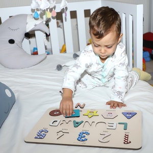 May include: A wooden puzzle with colourful shapes and numbers. The puzzle features the name "Leonard" and the words "one", "two", "three", "four", "five". A young child is playing with the puzzle.