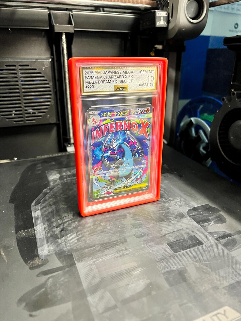 May include: A graded Japanese Mega Charizard X EX card in a red protective case. The card features the text "INFERNOX" and other Japanese text. The case is graded GEM-MT 10 by AGS.