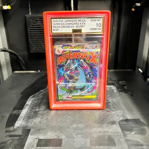 May include: A graded Japanese Mega Charizard X EX trading card in a red protective case. The card features a colorful illustration of a dragon-like creature with the text "INFERNOX". The case has a GEM-MT 10 grade.