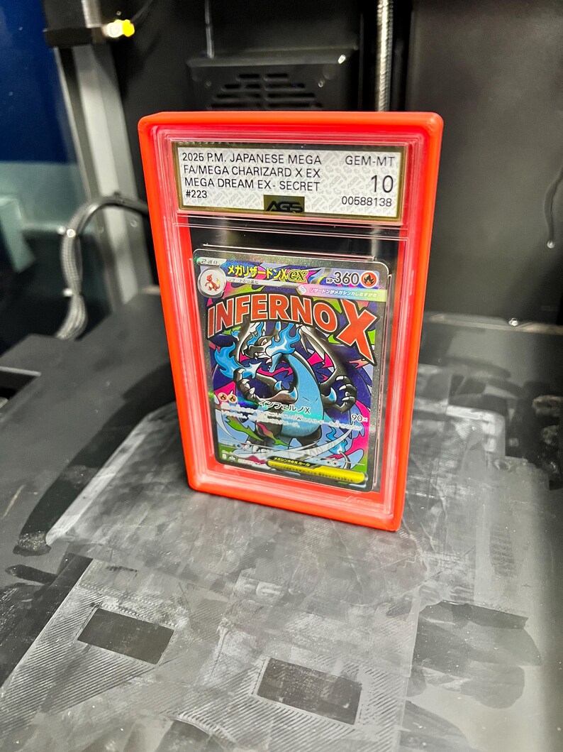 May include: A graded trading card in a clear plastic case with an orange frame. The card features a colorful illustration of a dragon-like creature with the text "INFERNO X". The case has text indicating it is a Japanese Mega Charizard card.