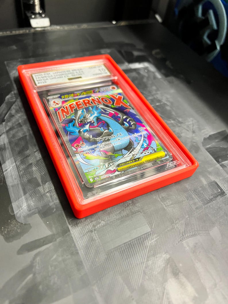 May include: A graded trading card in a red plastic case. The card features a colorful illustration of a blue and black creature with the word "InfernoX" in red and yellow. The card is graded a 10.