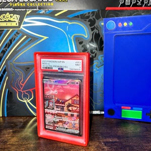 May include: A graded Pok&eacute;mon card featuring Mew ex, encased in a red holder. The card displays a colorful illustration of Mew and a town scene. The holder is labeled with the card's details, including the set and grade.