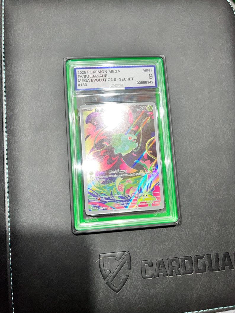 May include: A graded Pok&eacute;mon card featuring a Mega Bulbasaur from the Mega Evolutions Secret set. The card is encased in a green holder with the text "MINT 9" and other details. The card art showcases a colorful illustration of Bulbasaur.
