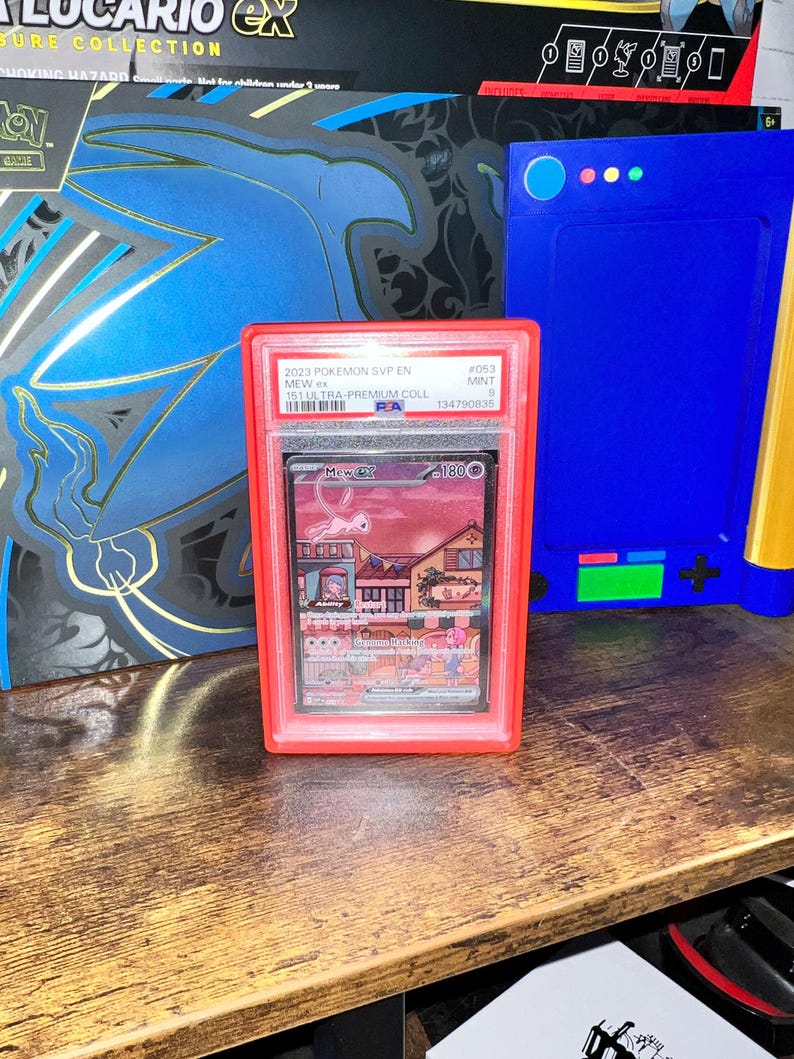 May include: A graded Pok&eacute;mon card in a red case. The card features the character Mew ex, with the text "2023 Pok&eacute;mon SVP EN" and "151 ULTRA-PREMIUM COLL". The case is labeled "MINT 9" and has a PA grading.