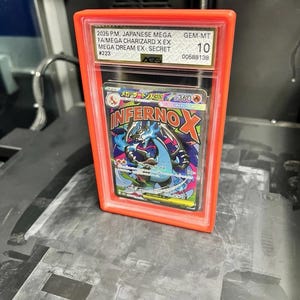 May include: A graded Japanese Mega Charizard X EX card in a red plastic case. The card is graded GEM-MT 10 by AGS. The card features the text "INFERNO X" and Japanese text.