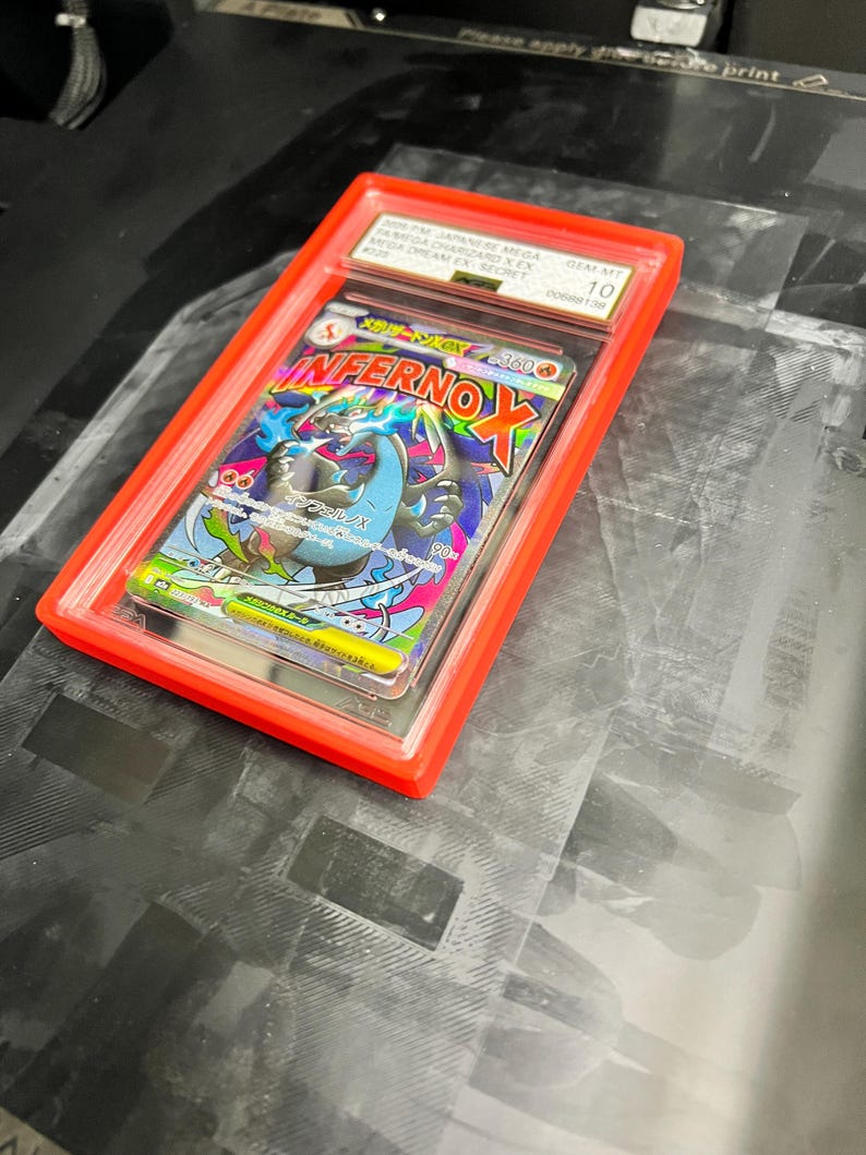May include: A graded trading card in a red plastic case. The card features a colorful illustration of a dragon with the text "Inferno X". The case is labeled with text including "GEM-MT 10".