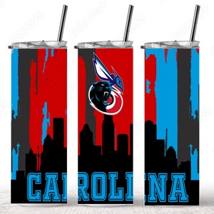 Puede incluir: Un vaso de acero inoxidable con un logotipo de los Carolina Panthers y un dise&ntilde;o de ciudad. El vaso es rojo, negro y azul con las palabras "CAROLINA" en azul.