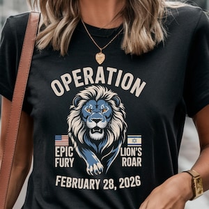 May include: Black t-shirt with the word "OPERATION" above a blue lion illustration. Below the lion are the words "EPIC FURY" and "LION'S ROAR" with the date "FEBRUARY 28, 2026". The American and Israeli flags are also present.