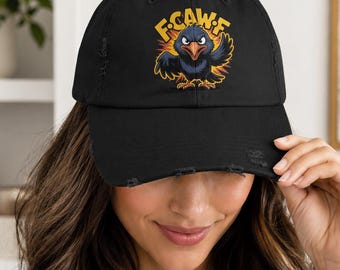 May include: Black distressed baseball cap featuring a cartoon crow with the text "F-CAW-F" in yellow. The crow is depicted with a fierce expression and outstretched wings, set against a yellow and orange burst.