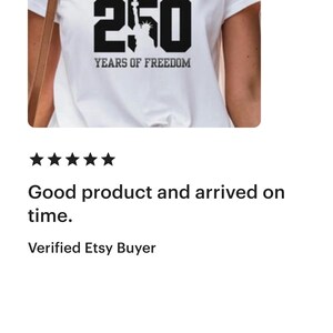 Puede incluir: Camiseta blanca con el texto "AMERICA 250 YEARS OF FREEDOM" en negro y gris. El n&uacute;mero 250 presenta una silueta de la Estatua de la Libertad. Un dise&ntilde;o sencillo y patri&oacute;tico.