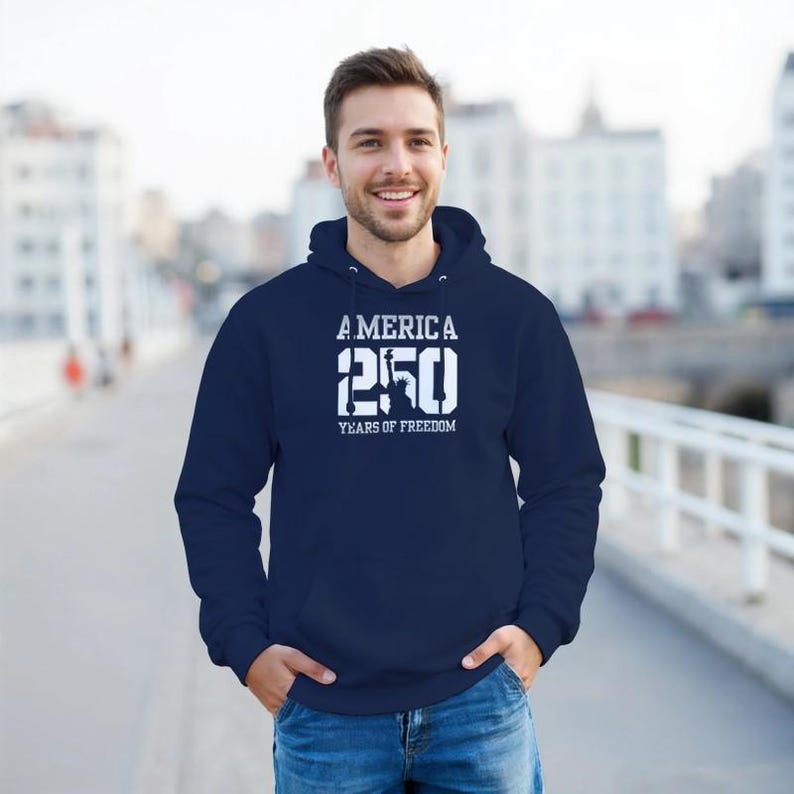 Puede incluir: Sudadera con capucha azul marino con el texto blanco "AMERICA 250 YEARS OF FREEDOM". La sudadera tiene una capucha con cord&oacute;n y un bolsillo delantero. La persona lleva vaqueros azules.