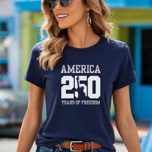 Puede incluir: Camiseta azul marino con el texto blanco "AMERICA 250 YEARS OF FREEDOM". El n&uacute;mero 250 est&aacute; en negrita, con la silueta de la Estatua de la Libertad. La camiseta tiene mangas cortas y cuello redondo.