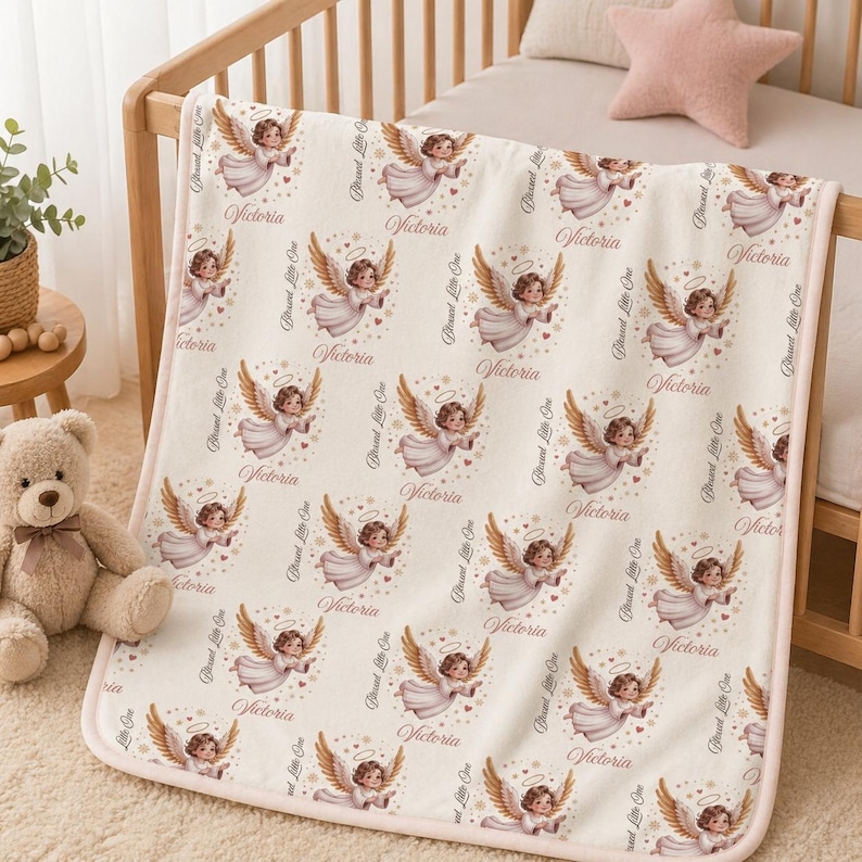 May include: A baby blanket with a repeating pattern of cherubic angels, each with golden wings and a halo. The name "Victoria" is printed above each angel, with the words "Blessed Little One" along the border. The blanket has a pink border.
