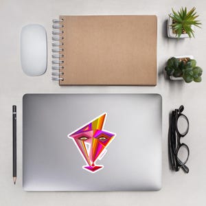 May include: A colorful abstract geometric design sticker featuring a stylized face with pink, orange, yellow, and red colors. The sticker is on a silver laptop.