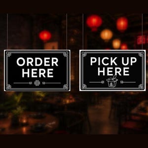 Op de afbeelding: Twee rechthoekige zwarte borden met witte tekst en randen. Het linkerbord bevat de tekst ORDER HERE met een decoratief symbool. Het rechterbord bevat de tekst PICK UP HERE met een afbeelding van een afhaalbakje en een geometrische rand.