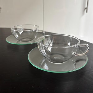 May include: Two clear glass teacups with matching saucers. The saucers have a green rim.