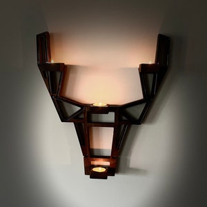 May include: A wooden wall-mounted candle holder shaped like a deer head with four candle holders. The candle holder is dark brown and has a geometric design.