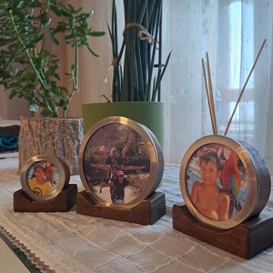May include: Three round picture frames with wood bases. The frames are gold with a silver trim. The photos in the frames are of people. The largest frame shows a family of four, the middle frame shows a young boy, and the smallest frame shows a young girl.