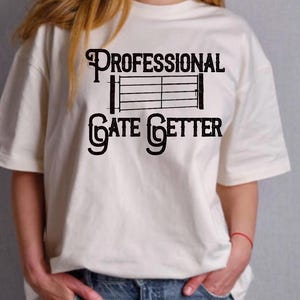 Könnte beinhalten: Cremefarbenes T-Shirt mit dem schwarzen Text "PROFESSIONAL GATE GETTER" und einer Tor-Grafik. Das Shirt hat kurze Ärmel und einen lässigen Stil.