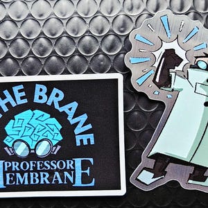 Könnte beinhalten: Zwei Aufkleber auf einer strukturierten schwarzen Oberfläche. Ein Aufkleber hat den Text "BE THE BRANE" über einer blauen Gehirngrafik mit Brille und "PROFESSOR MEMBRANE" darunter. Der andere Aufkleber ist ein Cartoon eines Wissenschaftlers im Laborkittel.