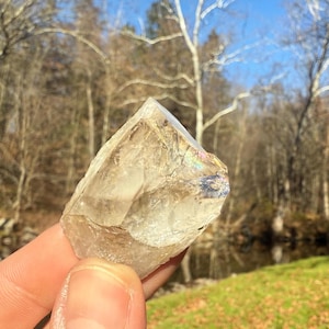 May include: A clear quartz crystal with iridescent rainbow colors. The crystal is rough and has a natural, irregular shape.