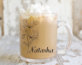 May include: A clear glass mug with a black floral design and the name "Natasha" printed on the side. The mug is filled with a brown beverage topped with white marshmallows.