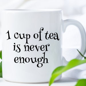 以下が含まれることがあります： 「1 cup of tea is never enough」という黒い文字が書かれた白いセラミックマグカップです。