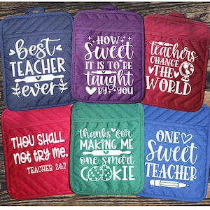 May include: Set of six colorful oven mitts with different teacher-themed sayings. The sayings include "Best Teacher Ever", "How Sweet It Is To Be Taught By You", "Teachers Change The World", "Thou Shall Not Try Me. Teacher 24/7", "Thanks For Making Me One Smart Cookie", and "One Sweet Teacher".