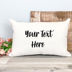 K&ouml;nnte beinhalten: Ein wei&szlig;es Kissen mit dem Text "Your Text Here" in schwarzer Kursivschrift.