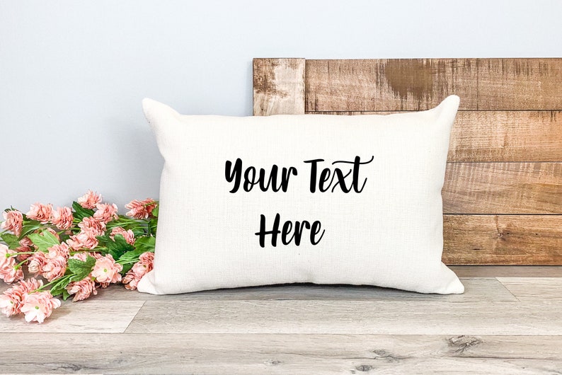 K&ouml;nnte beinhalten: Ein wei&szlig;es Kissen mit dem Text "Your Text Here" in schwarzer Kursivschrift.