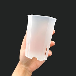 Könnte beinhalten: Ein durchsichtiger Plastiktopf mit rechteckiger Form. Der Topf hat eine matte Oberfläche und ist für kleine Pflanzen gedacht.