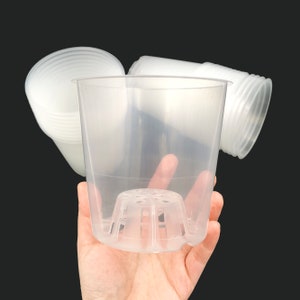 Pode incluir: Vasos de plantas de plástico transparente com base perfurada para uma drenagem ideal. A imagem mostra vários vasos, alguns empilhados, com foco no material transparente e no design da base. Adequados para várias plantas.
