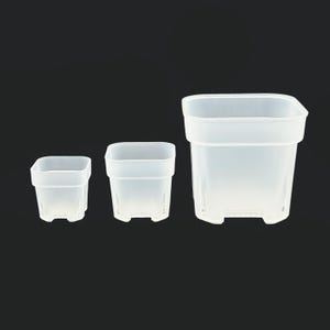 Op de afbeelding: Drie transparante, vierkante plastic bloempotten van verschillende formaten tegen een zwarte achtergrond. Elke pot heeft een licht uitlopende rand en kleine voetjes. De doorschijnende potten laten licht door.